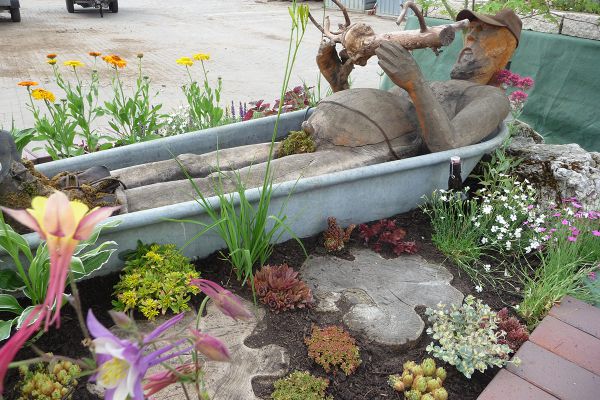 Kreative Gartenidee von Galabau Neundörfer mit Holzskulptur und liebevoll bepflanztem Beet